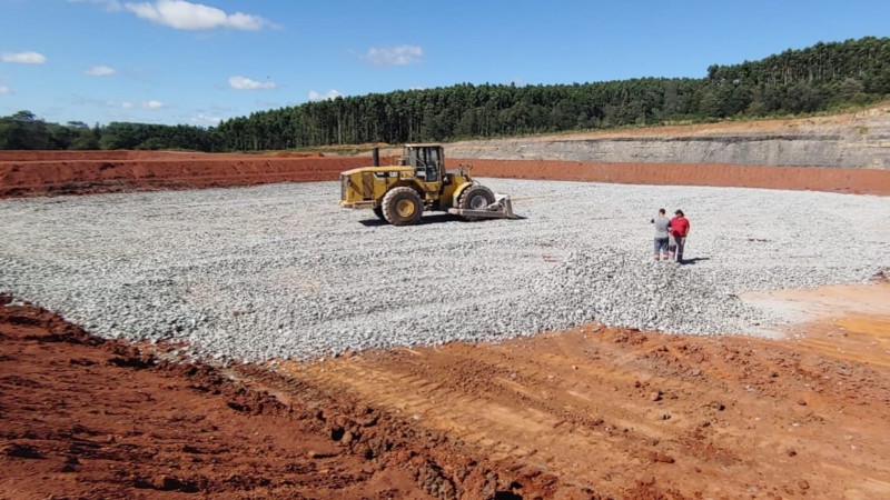 A imagem mostra a construção das Estações de Tratamento de Efluentes (ETEs) na região de Candiota. Em primeiro plano, um trator de grande porte está posicionado sobre uma área de terraplanagem. O fundo apresenta um panorama da área em desenvolvimento, com pode-se notar o início da estrutura das ETEs. O céu está limpo e há pouca vegetação ao redor, evidenciando o foco nas obras de infraestrutura. A cena transmite a ideia de progresso e melhorias na gestão de efluentes na região.