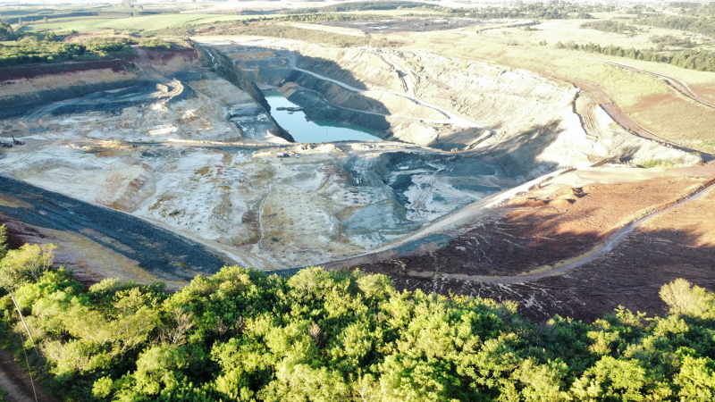 A imagem da Mina São Vicente Norte, apresenta uma paisagem industrial com vastas áreas de extração. A cena é marcada pela presença de vegetação ao redor, que pode ser afetada pela atividade mineradora. Esta imagem ilustra a relação entre a extração mineral e o meio ambiente