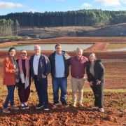  Seis pessoas da equipe da CRM (Companhia Riograndense de Mineração) estão reunidas em uma área de mineração a céu aberto em Candiota. Todos usam roupas normais. Ao fundo, é possível ver as áreas novas mineradas. O grupo está sorrindo e posicionado lado a lado, demonstrando união e profissionalismo no ambiente de trabalho.