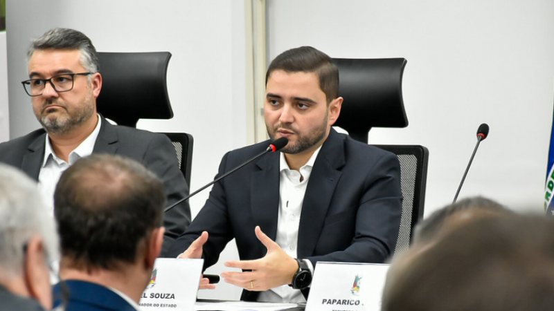 O secretário adjunto Marcelo Camardelli e o vice-governador Gabriel Souza estão sentados lado a lado em uma mesa de reunião. Ambos usam ternos escuros e estão concentrados, observando ou escutando atentamente durante a discussão.