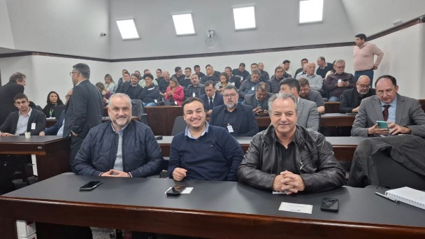 Três pessoas estão sentadas lado a lado em uma mesa de reunião, sorrindo para a foto.São elas, presidente Ademir Baretta, superintendentes de Candiota, Murilo e Gildo Feijo, Todos vestem roupas escuras, condizentes com o ambiente institucional. Estão posicionadas em frente a uma mesa de reunião. O clima entre elas parece descontraído e cordial, contrastando com o caráter técnico do encontro sobre o futuro energético. Ao fundo, pode-se ver parte do plenarinho, na assembleia legislativa do estado do RS, com iluminação clara.