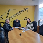 Três pessoas sorrindo durante uma reunião em um ambiente vibrante e amarelo, transmitindo uma atmosfera amigável e energizante.
