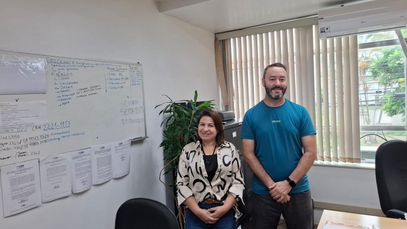 A imagem mostra os dois funcion&aacute;rios; Anderson e Rocheli lado a lado numa sala de trabalho onde tem um quadro branco escrito coisas de trabalho. Os funcion&aacute;rios est&atilde;o alegres porque est&atilde;o numa nova fun&ccedil;&atilde;o na sede da CRM em Porto Alegre