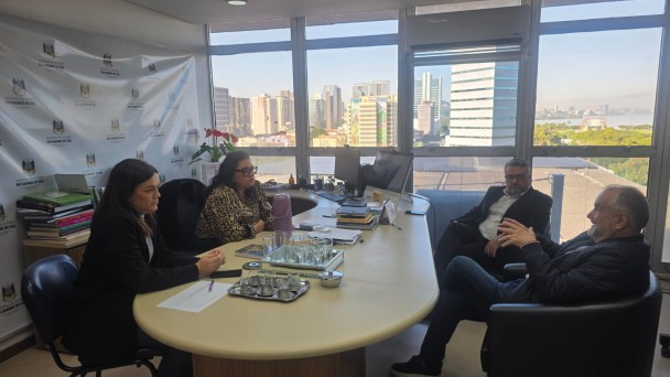 Numa sala ampla com uma mesa em formato retangular est&atilde;o sentados 4 autoridadades da SEMA e CRM, atr&aacute;s de onde est&atilde;o sentadas tem um banner do governo do estado , conversando amigavelmente as 4 pessoas. 