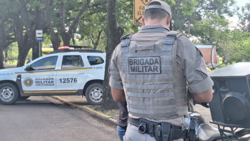 Na imaem mostra de costas um profissional vestido de PM da Briaa Militar e uma viatura &agrave; sua frente. 