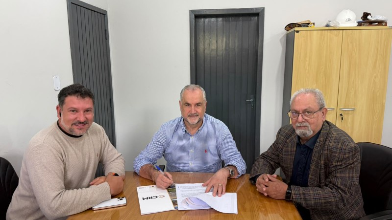 A imagem mostra os 3 homens em quest&atilde;o, o presidente da CRM Ademir Baretta no meio dos dois com a caneta assinando a cess&atilde;o de comodato, do seu lado esquerdo, o diretor Jo&atilde;o Batista Alves Rodrigues e do seu lado direito o Vice-Prefeito Daniel Oliboni de Minas do Le&atilde;o. Todos est&atilde;o sorridentes na foto olhando para a c&acirc;mera.